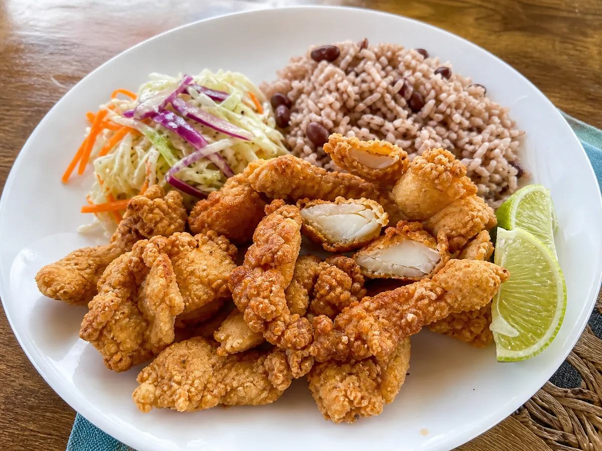 Golden Bahamian cracked conch with tender white conch visible, peas and rice, coleslaw and lime.