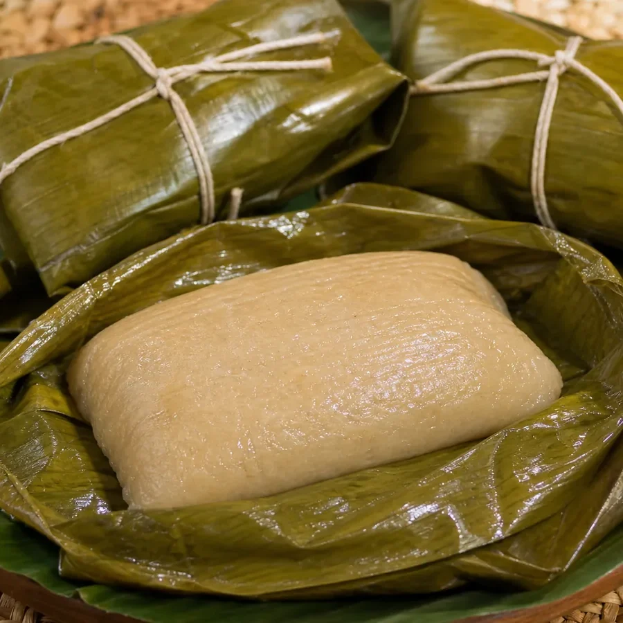 Jamaican duckunoo opened from a banana-leaf parcel beside two traditionally tied parcels.